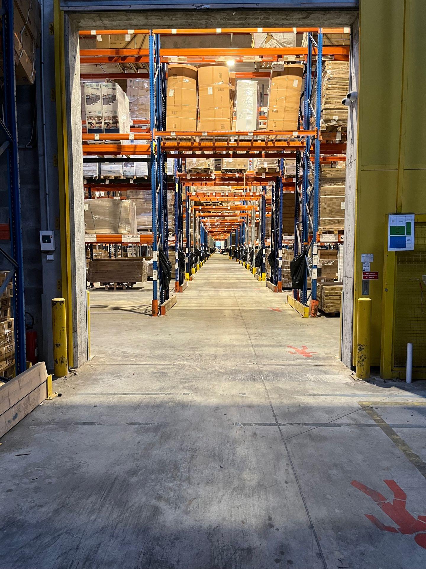 Long aisle in a large warehouse with high shelves stocked with pallets and boxes on both sides.