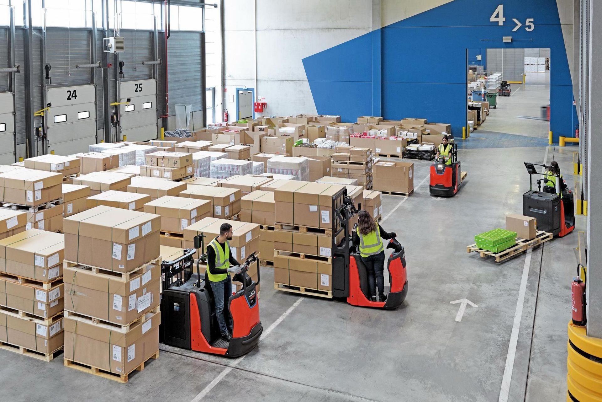 Warehouse workers using forklifts to move pallets of boxes in a large storage facility.